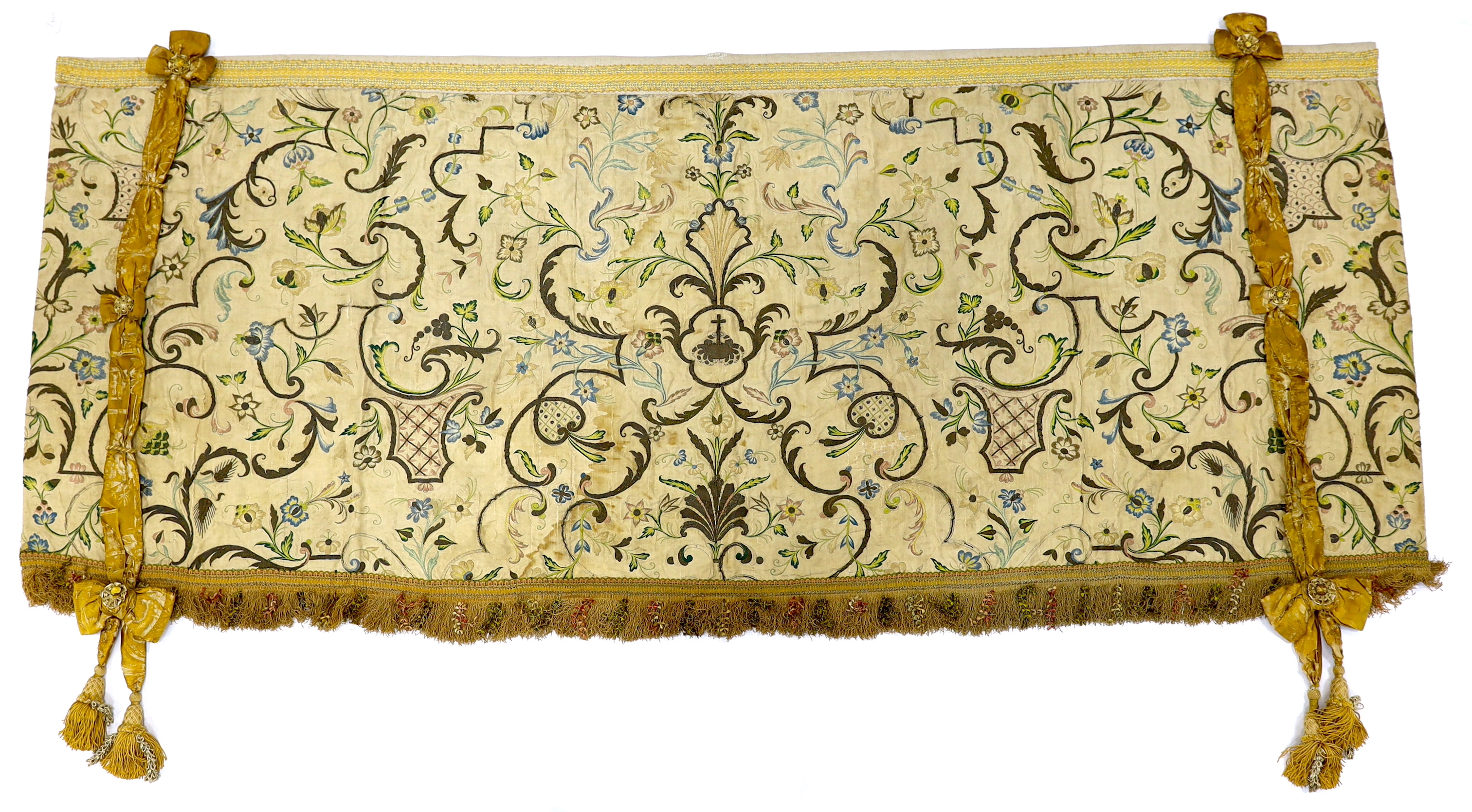 A mid-18th century Continental silk embroidered altar cloth, embroidered with polychrome silks and silver metallic threads in an all-over floral design on cream silk with ornate silk tasselling, (the damask tie backs add